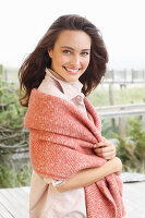 A young brunette woman wearing a light shirt blouse with a salmon pink woollen shawl