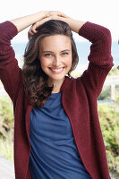 Junge brünette Frau in blauem Shirt und weinroter Strickjacke