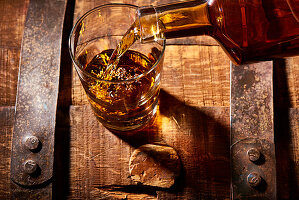 Bourbon in Glas mit Eiswürfeln auf Whiskeyfass einschenken