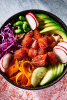 Poke bowl from overhead with gray stone surface on top and red mottled surface below