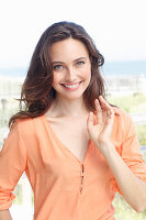 A young brunette woman wearing a salmon-pink tunic blouse