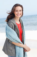 A young brunette woman wearing a red blouse, a grey windbreaker and a woollen shawl