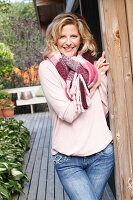 A blonde woman wearing a pink blouse, a thick scarf and jeans