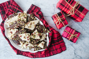 Dark and white chocolate bark with cranberries and pistachios on a dish with small wrapped presents