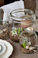 Gläser mit Nestern aus Heu mit Blumen und Eierschalen