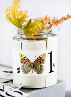 Schmetterling-Motiv auf Papiermanschette um ein Glas mit Duftgeranienblättern