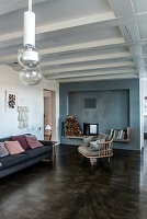 A cosy chair and a sofa on a concrete floor in front of a fireplace in a blue wall