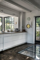Weiße Unterschränke vor Fenster und Boden mit Glaseinsatz in der Küche