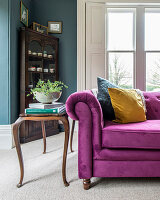 Old side table next to pink velvet sofa in classic living room