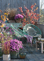 Herbstbalkon mit Chrysanthemen, Liebesperlenstrauch, Schneeball und Gräsern, Sessel mit Fell und Decke