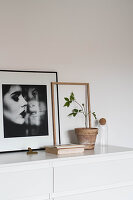 Framed portrait of woman next to potted plant on white chest of drawers