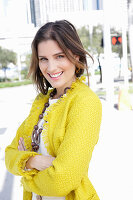 A young woman wearing a chunky necklace and a yellow bouclé jacket
