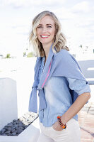 A blonde woman wearing a denim shirt with a jumper over her shoulders