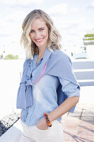 A blonde woman wearing a denim shirt with a jumper over her shoulders