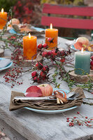 Autumn table decorations with rose hips, candles and apples