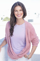 Junge Frau mit langen Haaren in fliederfarbenem T-Shirt und Wickel-Pullover