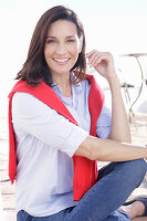 Brünette Frau in hellem Hemd und mit rotem Pullover über den Schultern