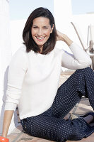 A brunette woman wearing a white jumper and polka dot trousers