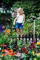 Mädchen gießt Blumen im eingezäunten Mini-Garten