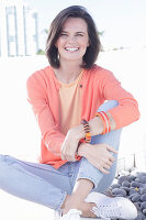 Junge Frau in apricotfarbenem Top mit Strickjacke und Jeans