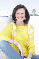 A young woman wearing a long-sleeved yellow top and jeans with a jumper over her shoulders