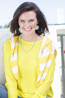 A young woman wearing a long-sleeved yellow top with a jumper over her shoulders