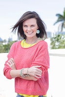 A young woman wearing large earrings, a fuchsia jumper and a yellow top