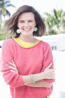 A young woman wearing large earrings, a fuchsia jumper and a yellow top