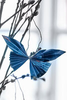 Blue folded paper butterfly hung from willow branch