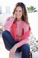 A long-haired woman wearing a pink top and jeans with a jumper over her shoulders