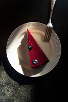 A piece of raspberry cake with two blueberries on a plate with a fork