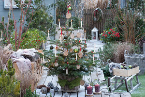 Nordmanntanne geschmückt mit Holzscheiben, Christbaumkugeln, Lichterkette und Kerzen, Brennholzstapel mit Fell und Decke als Sitzplatz