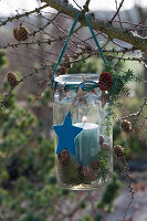 Mason jar hung on a larch branch as a lantern, decorated for Christmas with stars and cones