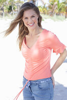 A long-haired woman wearing a short-sleeved salmon-coloured top and jeans