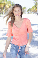 A long-haired woman wearing a short-sleeved salmon-coloured top and jeans