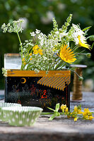 Sträußchen aus Blüten von Zwergalant, Hornklee, Ziersalbei und Wiesenkümmel in Teedose