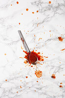 A spoon with splatter of tomato sauce on a marble surface