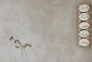 Bemalte Ostereier und Gräserblüten auf grauem Untergrund