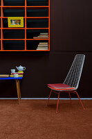 Metal chair below orange shelves on brown wall