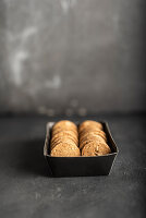 Dinkelplätzchen mit Mandeln in Schachtel vor grauem Hintergrund