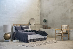 Double bed, bamboo chair and large table lamp on floor in room with grey walls