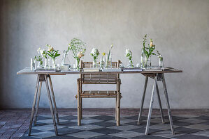 Rustikaler Holztisch mit Blumen in verschiedenen Glasgefäßen