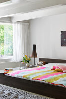 Double bed with striped bedspread next to window in bright bedroom