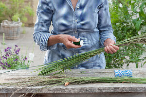 Riesenbrezel aus Gras binden Frau umwickelt mit Draht versteiftes Bund aus Gräsern mit feinem Wickeldraht