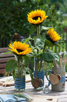 Tischdekoration mit Sonnenblumen, Holz-Herzen und Besteck im Bierkrug