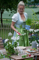 Frau deckt Tisch für die bayrische Brotzeit: Teller mit Radieschen und Brezeln auf Holzscheiben, Topf mit Schnittlauch und Bierkrug