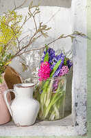 Vases of mimosa, hyacinths and hazel branches in niche in green wall