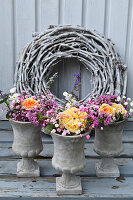 Summer bouquets of roses, Caucasian crosswort and gypsophila in small concrete urns in front of wreath of white-painted vines