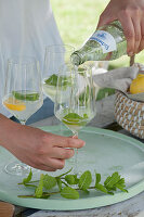 Frau füllt Gläser mit Mineralwasser, frische Minze und Orangenscheibe