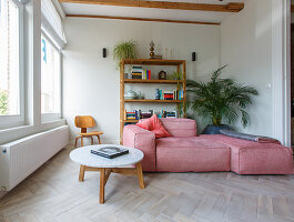 Pink sofa set in front of shelves, round coffee table and herringbone parquet flooring in living room